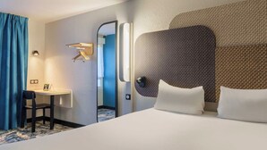 A hotel room with a large bed, a desk with a chair, a mirror, and a wall-mounted light fixture. - B&B HOTEL Troyes Centre (Troyes)