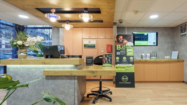 A reception desk with a laptop, a plant, and a B&B CLUB sign. - B&B HOTEL Troyes Centre (Troyes)