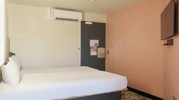 Una camera d'albergo con un letto, un condizionatore d'aria, una porta con un calendario e una televisione a parete.
