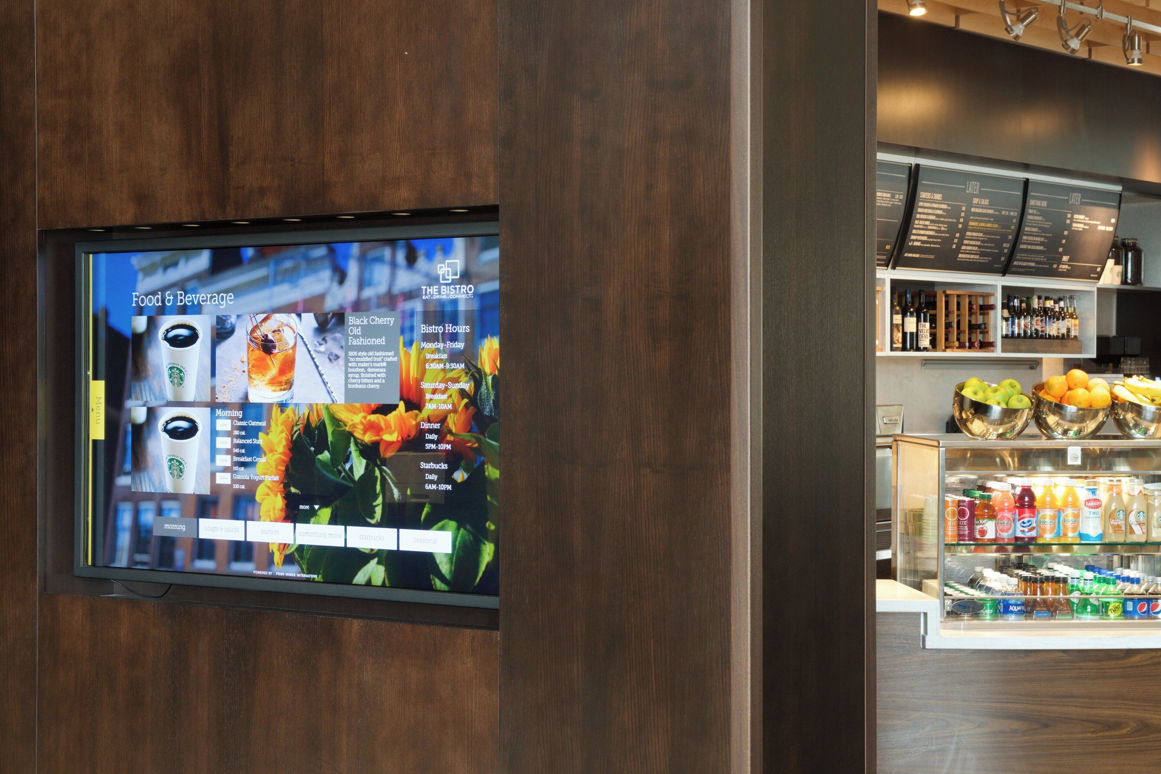 A digital menu board displaying food and beverage options, including Starbucks and Black Cherry Old Fashioned, in a restaurant setting.