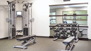 Un gimnasio con máquinas de pesas, mancuernas y un reloj digital.