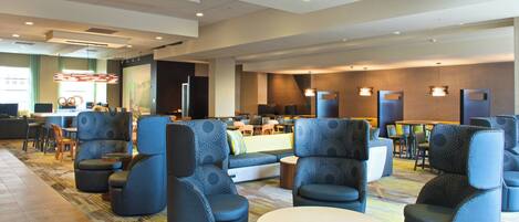 A modern lobby with seating areas, a reception desk, and a large mural on the wall.
