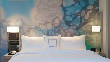 A hotel room with a large bed, two bedside lamps, a nightstand with a phone, and a wall with a textured abstract design.