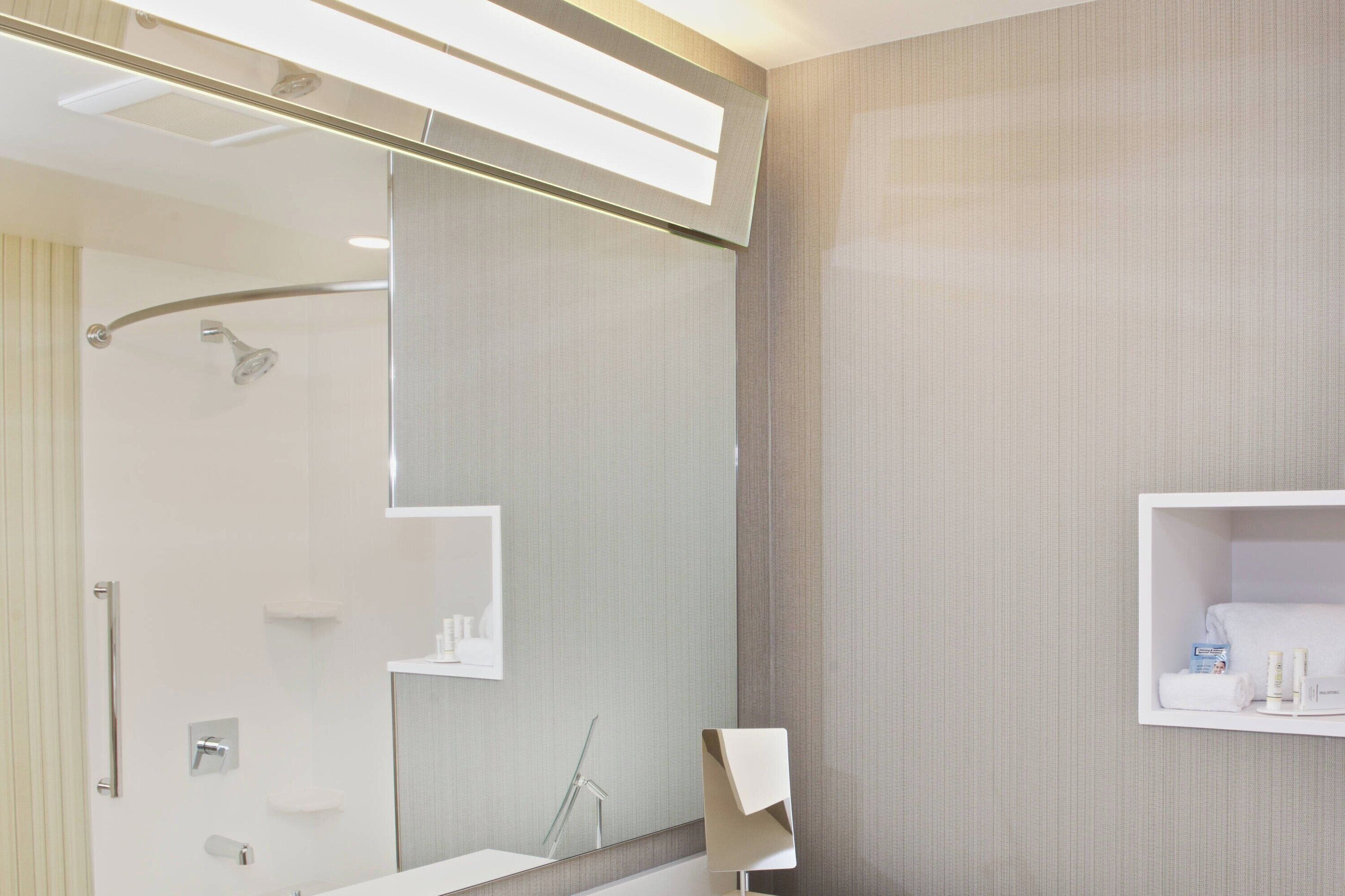 Un baño moderno con un espejo grande, ducha y tocador con perchero.