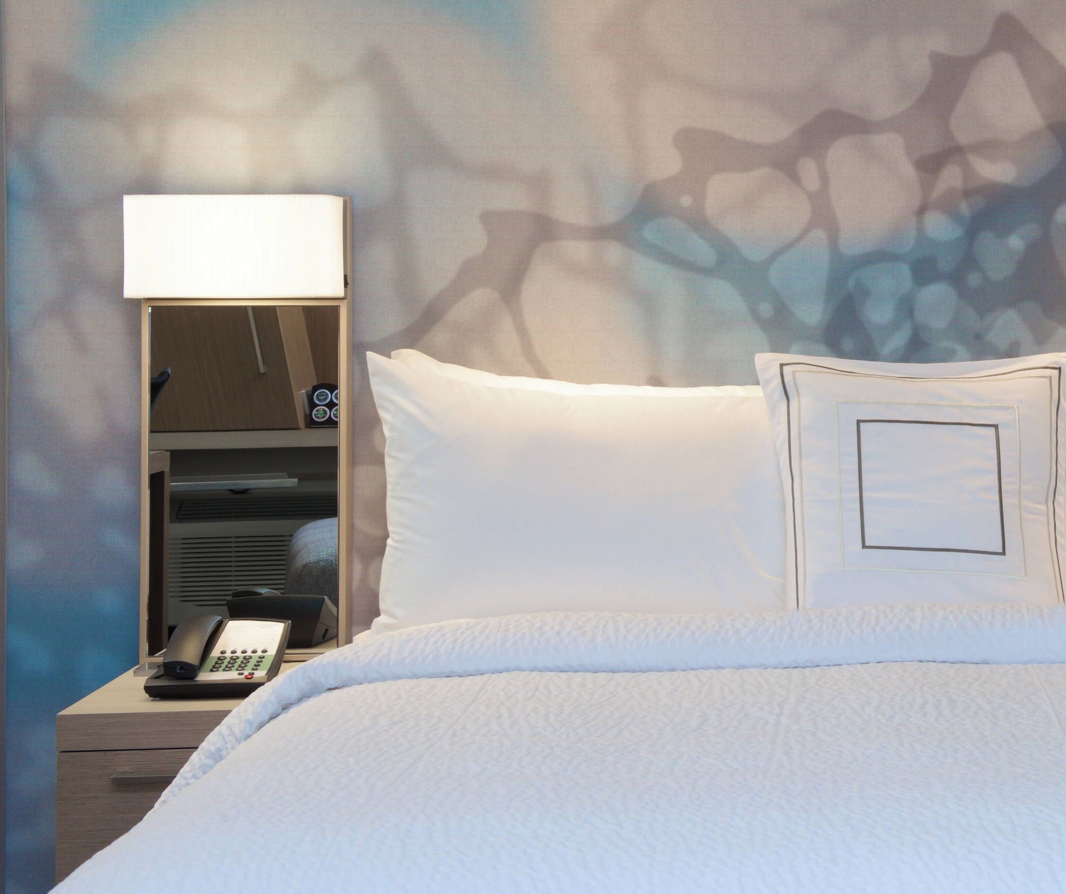 A hotel room with a bed, a bedside lamp, a telephone, and a wall with a textured pattern.