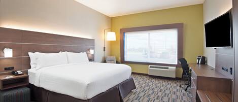 A hotel room with a large bed, a desk, a chair, a TV, and a window with a city view.