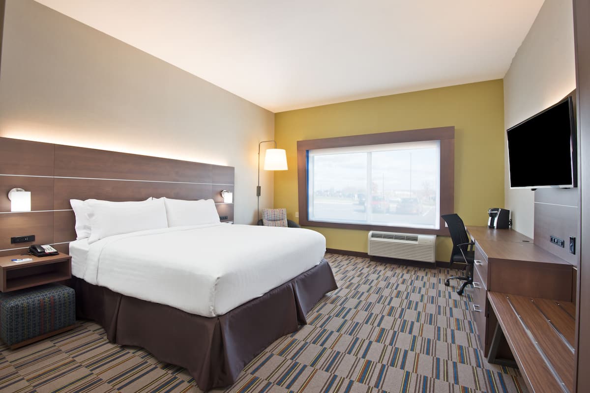 A hotel room with a large bed, a desk, a chair, a flat-screen TV, and a window with a city view.