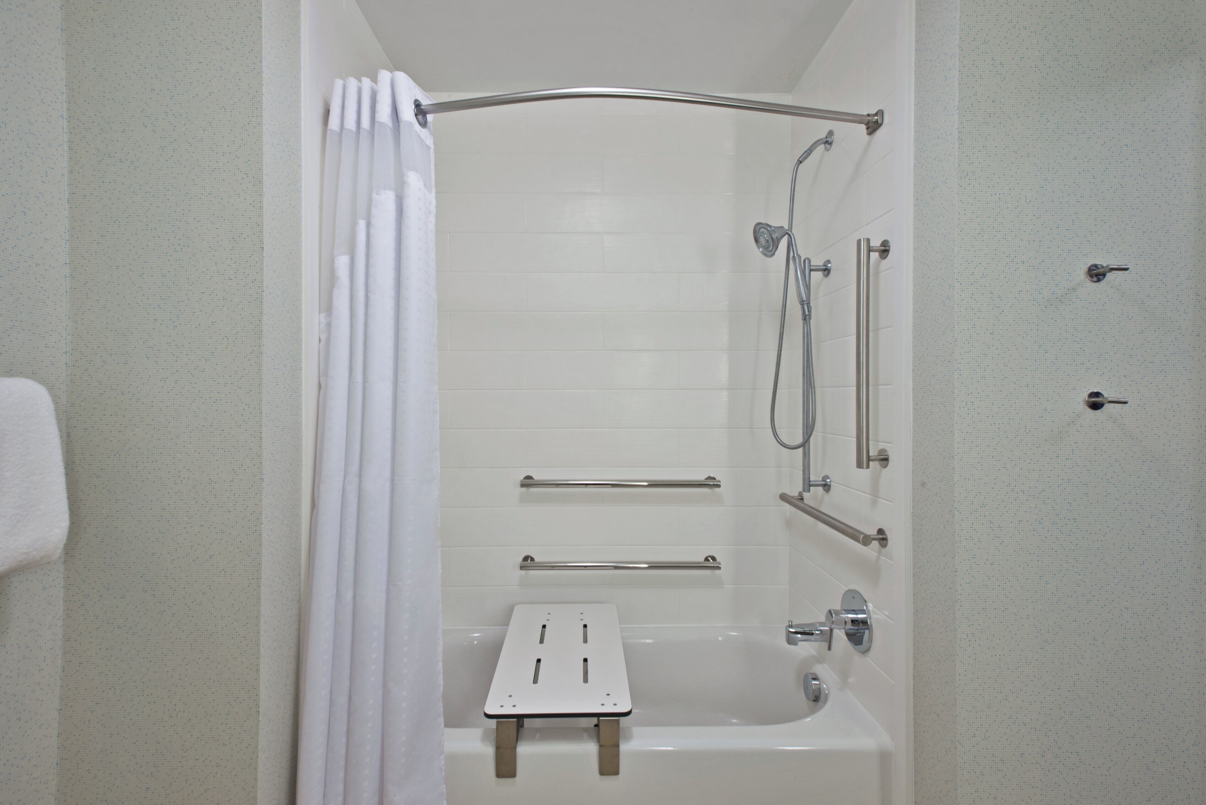 Un baño con bañera, ducha, barras de apoyo y perchero para toallas.