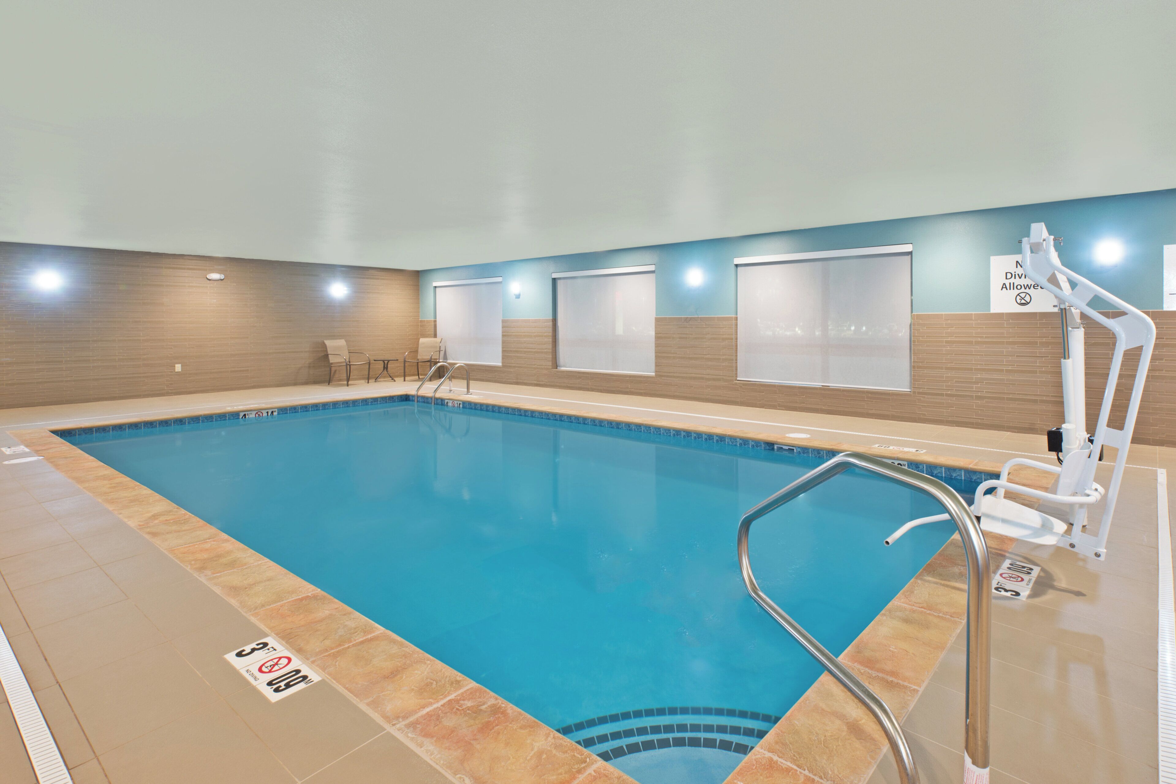 Una piscina interior con borde de azulejos, una escalera de piscina y un banco.