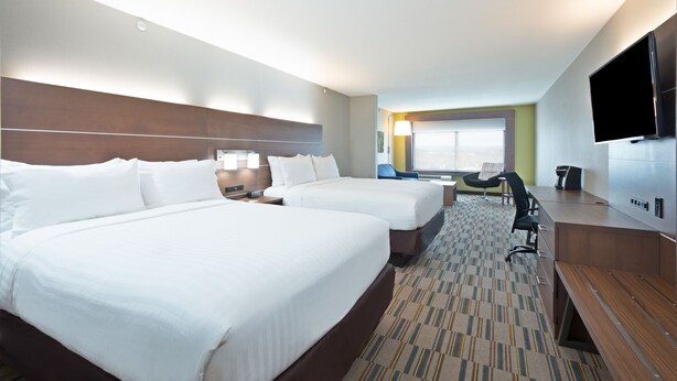A hotel room with two beds, a desk, a chair, a TV, and a window with a view.