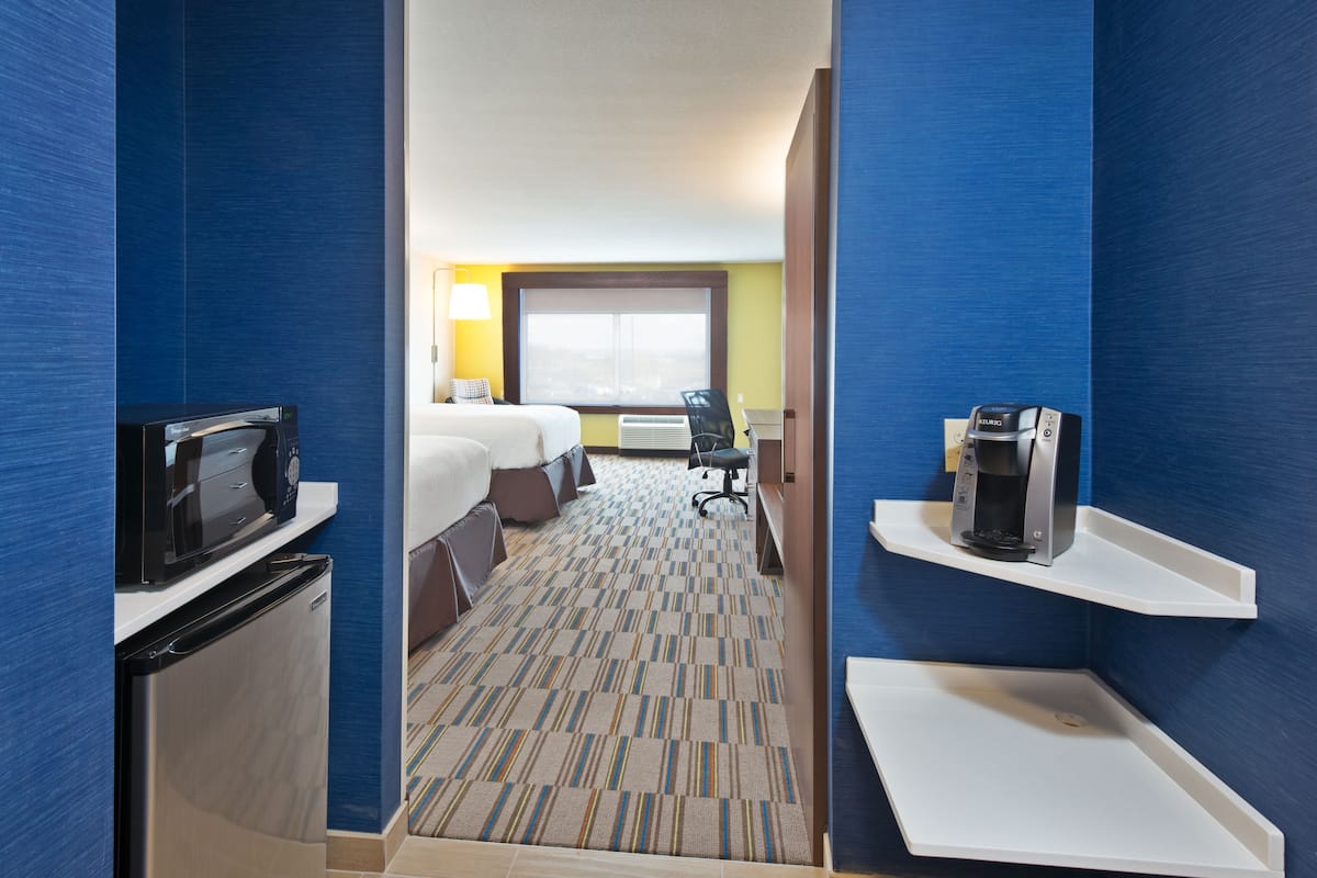 A hotel room with a bed, a desk, a chair, a microwave, a coffee maker, and a TV.