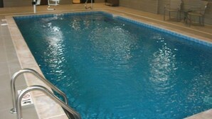 An indoor swimming pool with a clear water surface, a metal ladder, and a tiled floor.