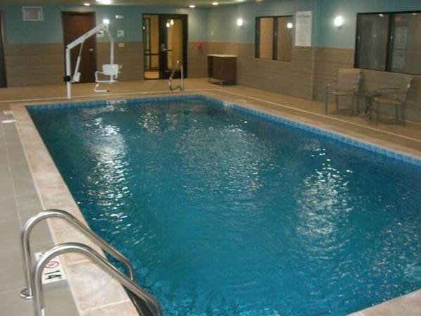 An indoor swimming pool with a clear water surface, a metal ladder, and a tiled floor.