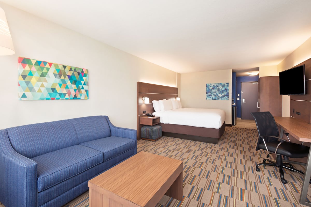A hotel room with a bed, a blue sofa, a wooden table, a desk with a chair, and a TV.