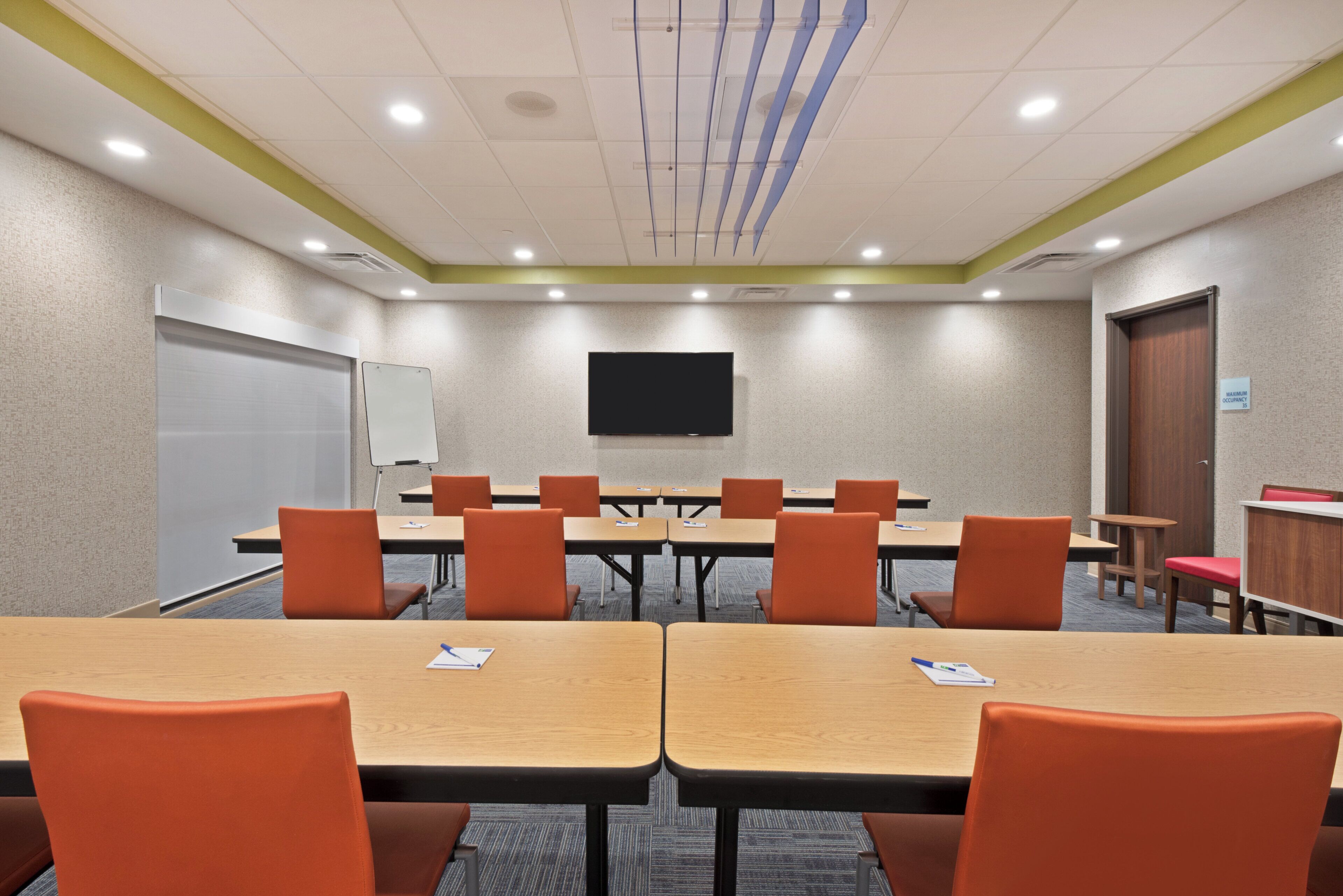 A conference room with tables and chairs, a whiteboard, and a television on the wall.