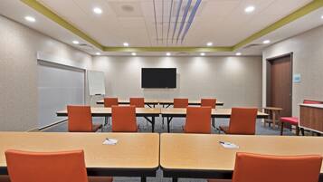 A conference room with tables and chairs, a whiteboard, and a television on the wall.