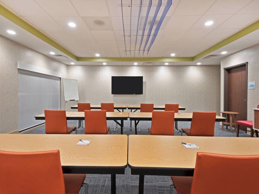 A conference room with tables and chairs, a whiteboard, and a television on the wall.