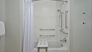 A bathroom with a bathtub, shower, and grab bars.