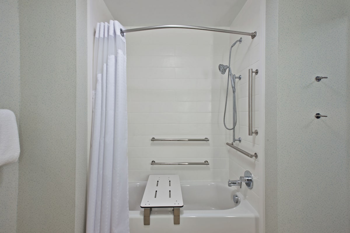 A bathroom with a bathtub, shower, and grab bars.