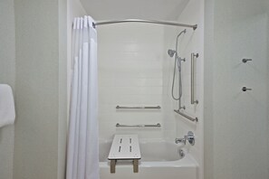A bathroom with a bathtub, shower, and grab bars.