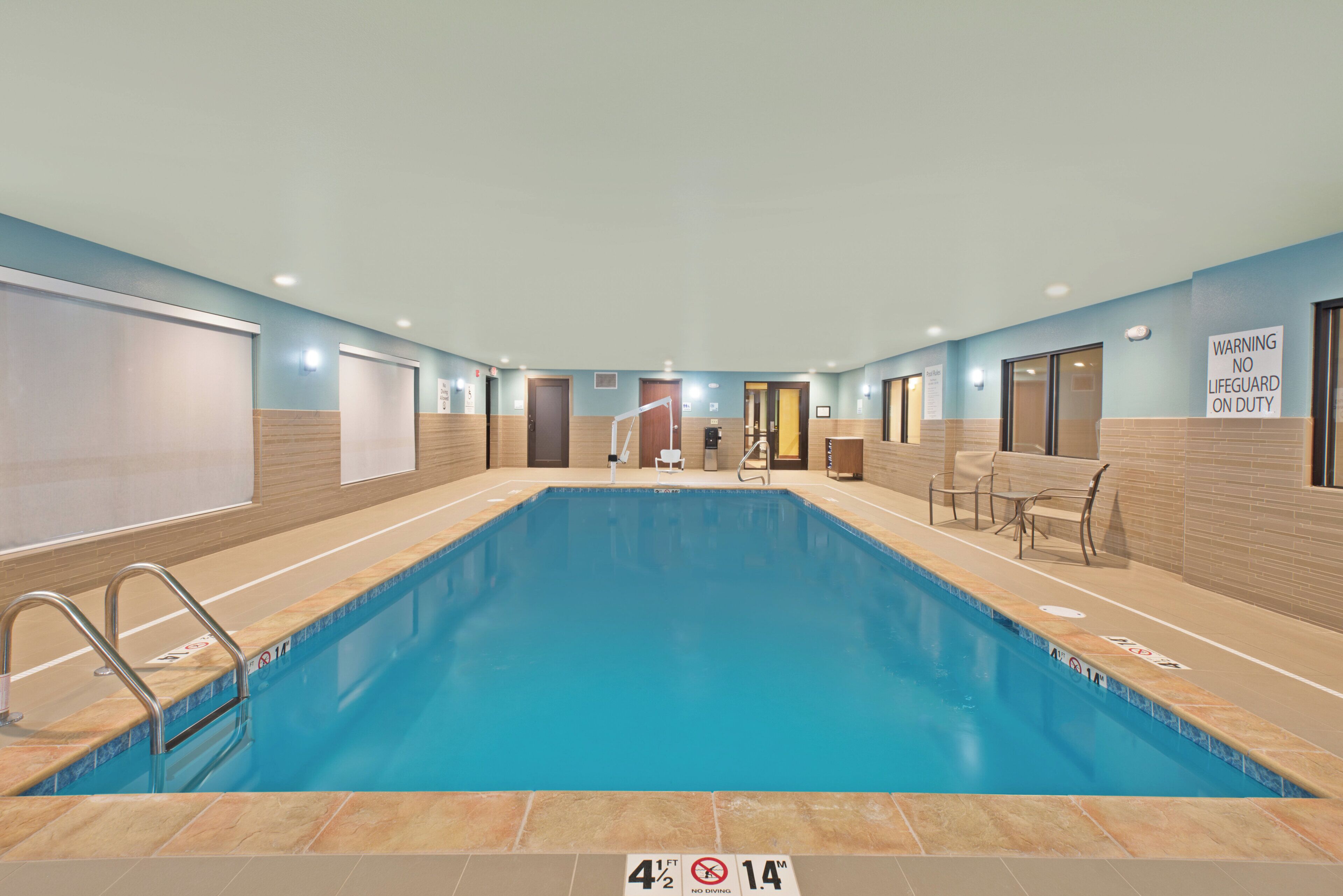 A swimming pool with a no diving sign, a lifeguard on duty sign, and a pool rules sign.
