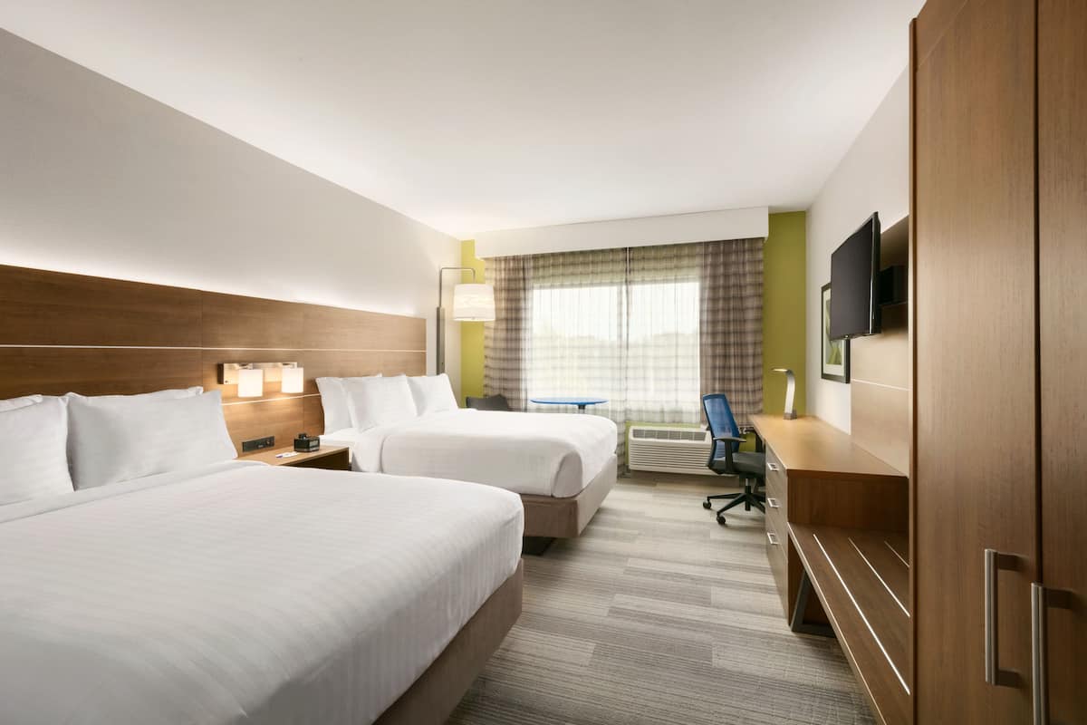 Habitación de hotel con dos camas, un escritorio, una silla, un televisor y una ventana con cortinas.
