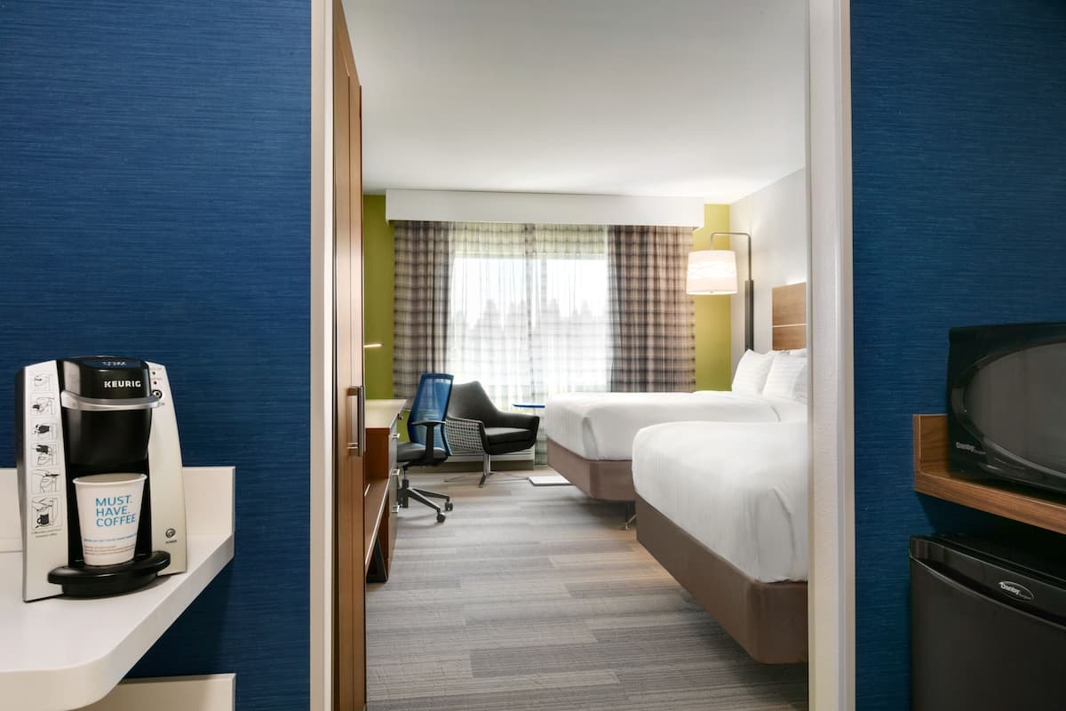 Una habitación de hotel con una cama, un escritorio con cafetera, una silla y un televisor.