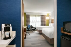 Een hotelkamer met een bed, een bureau met koffiezetapparaat, een stoel en een televisie.