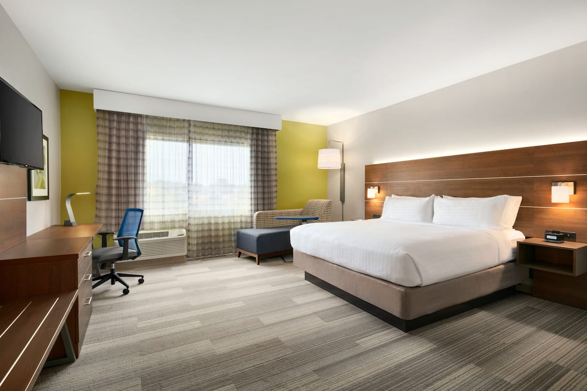 Habitación de hotel con una cama grande, un escritorio con silla, una mesita y un televisor.