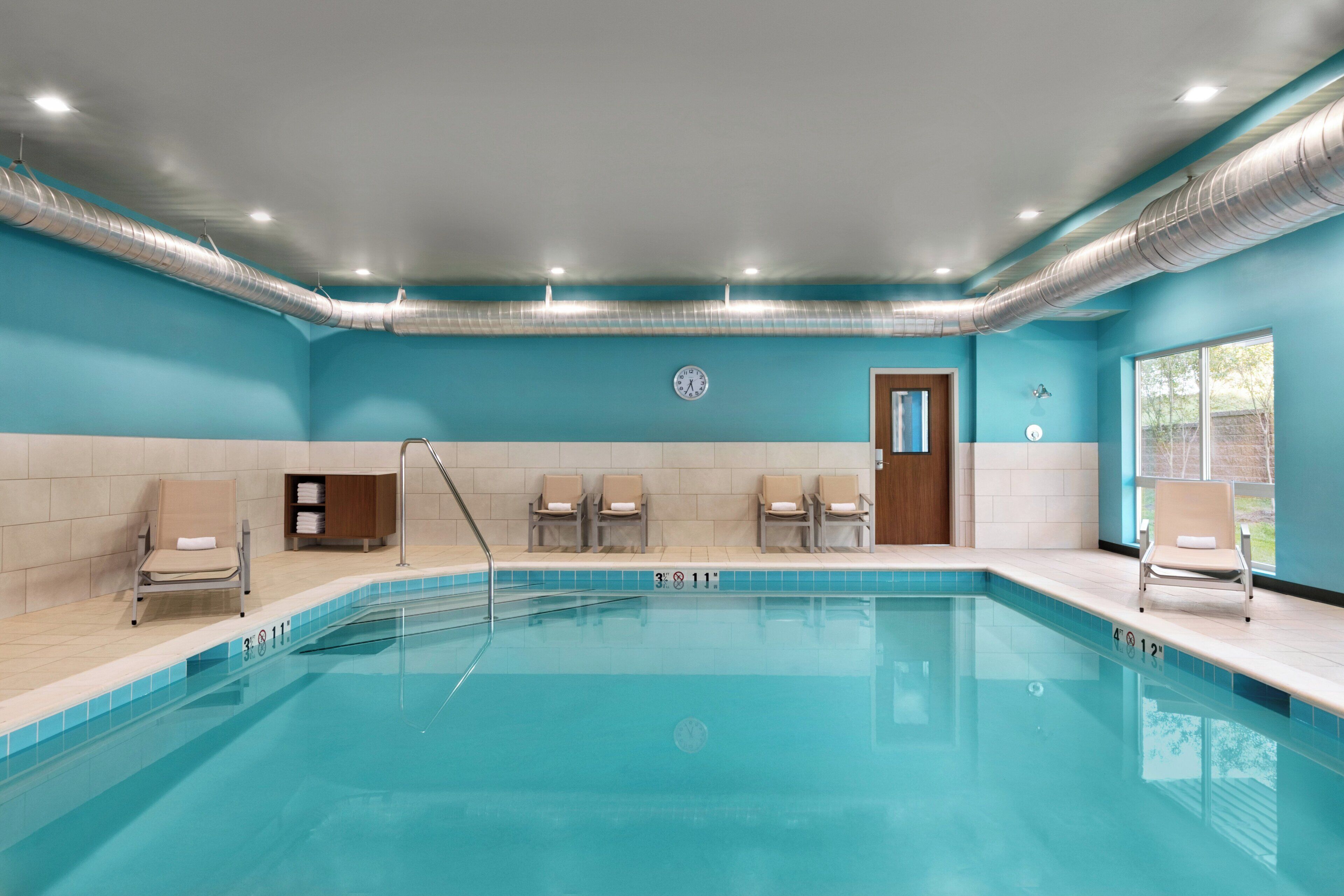 Uma piscina com um deck ladrilhado, cadeiras de descanso, um armário de madeira e uma porta.