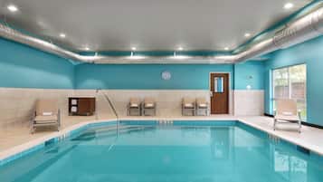 Uma piscina com um deck ladrilhado, cadeiras de descanso, um armário de madeira e uma porta.