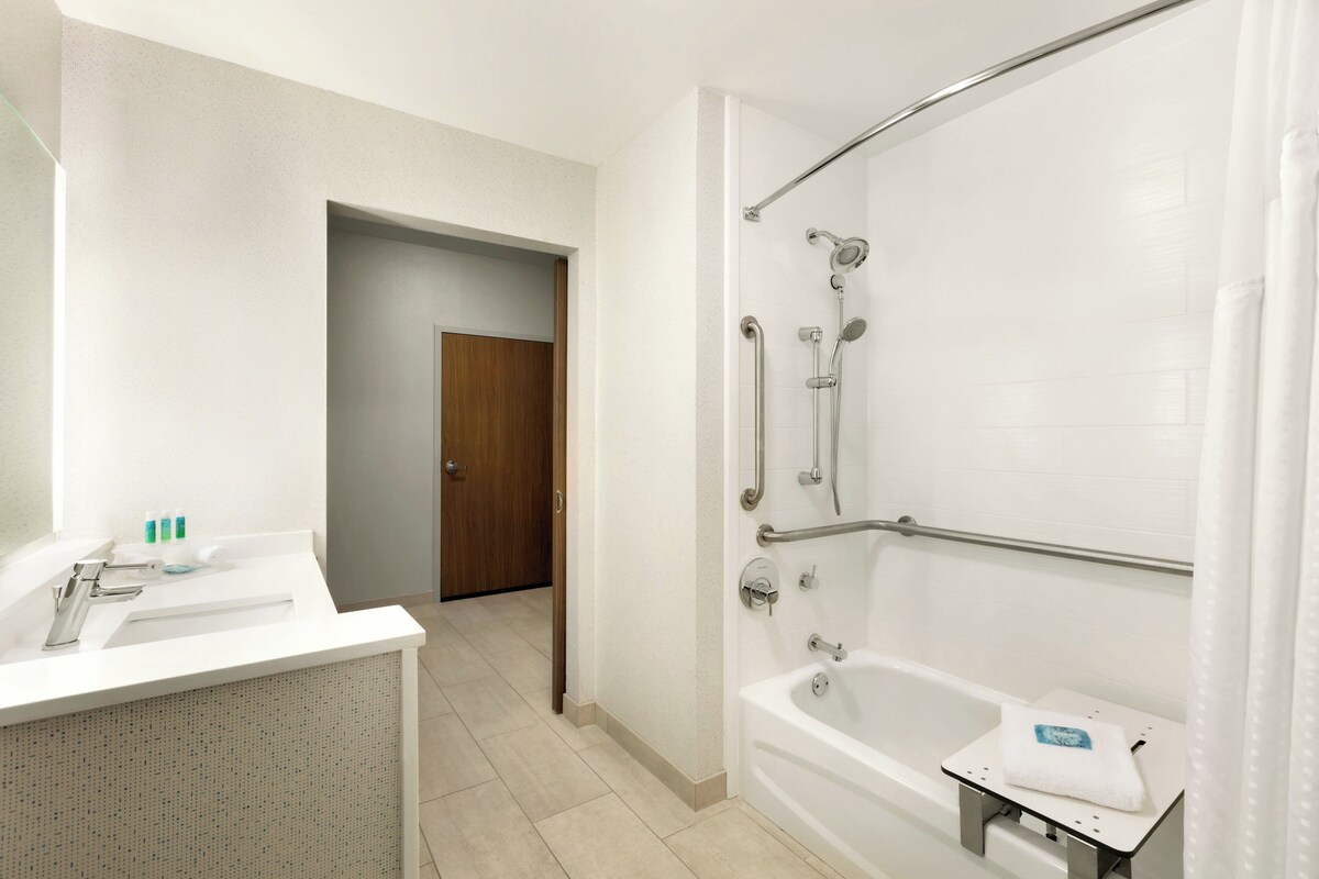 Een badkamer met een wit wastafel, spiegel en douche met handgrepen.