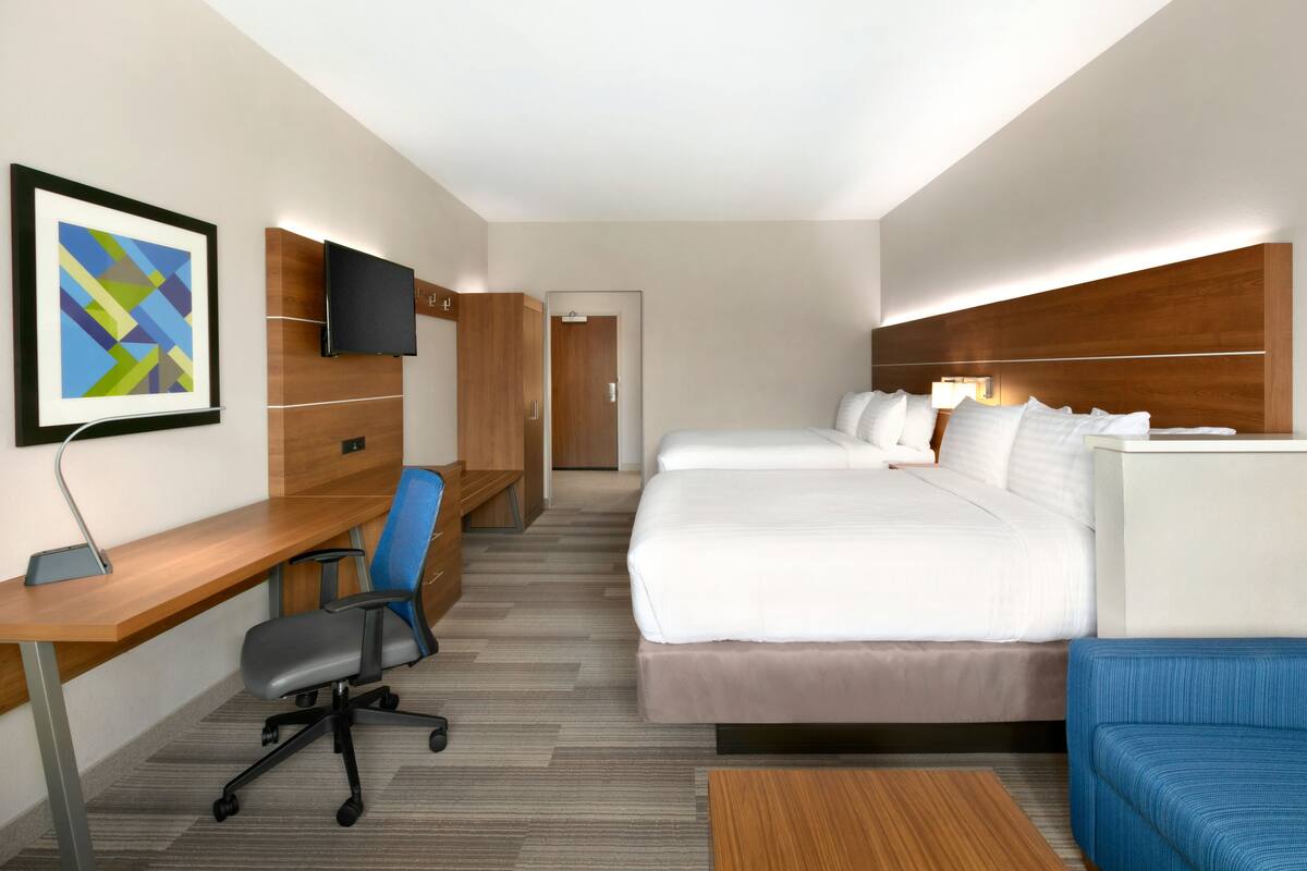 Habitación de hotel con cama, escritorio con silla, televisor montado en la pared y cabecero de madera.