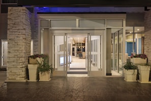 Entrada de hotel con un camino de ladrillo que lleva a una puerta de cristal.
