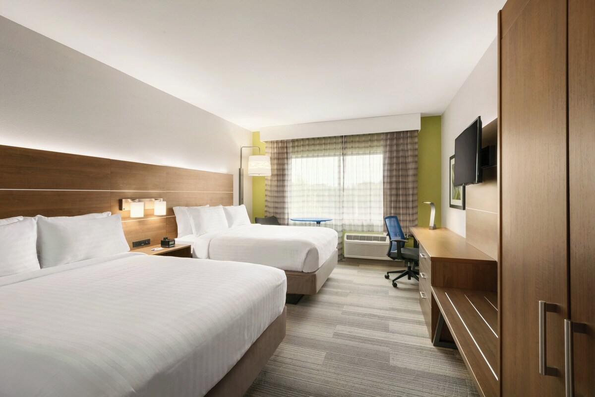 Een hotelkamer met twee bedden, een bureau met een computer, een televisie en een raam met gordijnen.