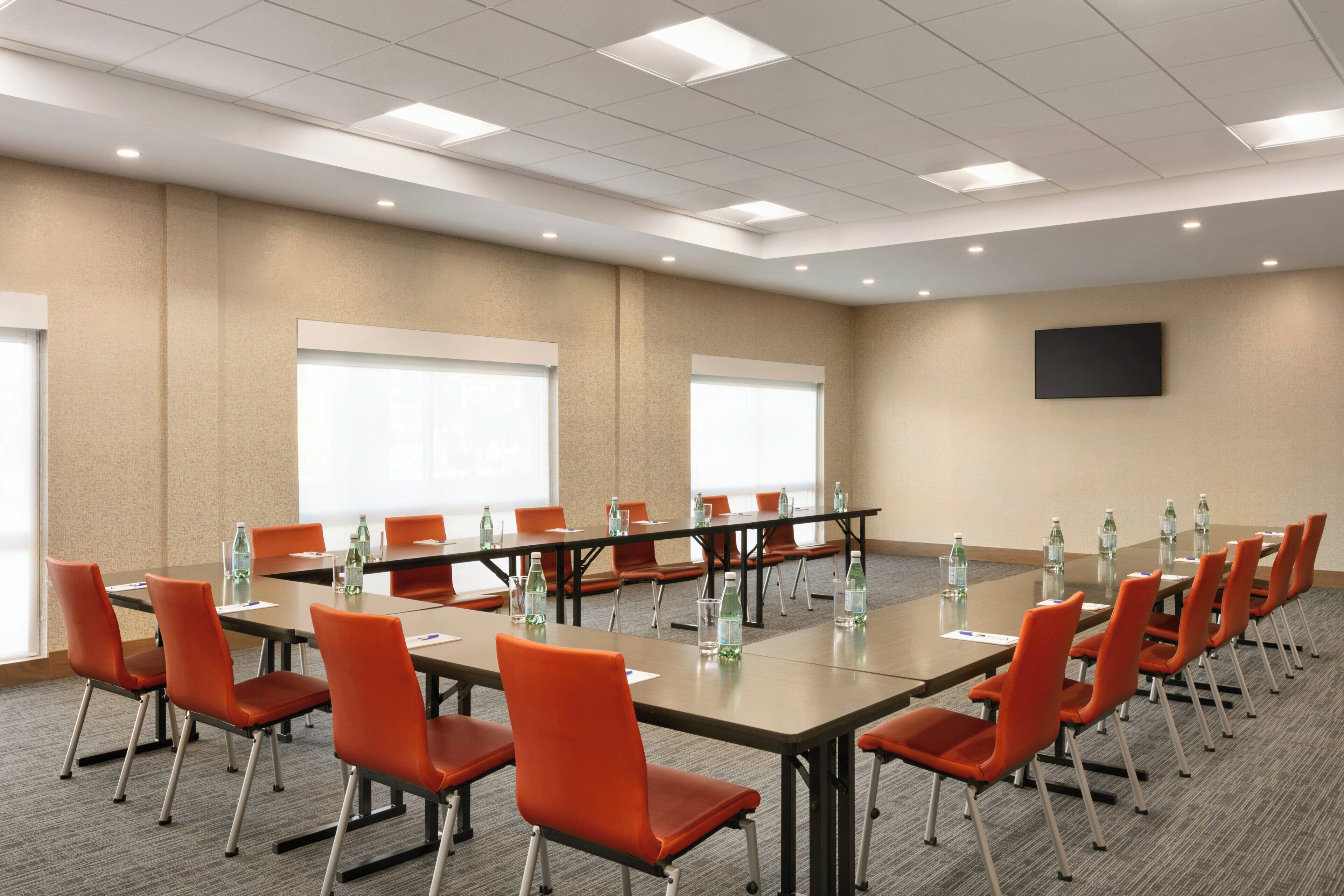 Un salón de conferencias con una larga mesa, sillas anaranjadas y botellas de agua.