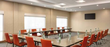 Un salón de conferencias con una larga mesa, sillas anaranjadas y botellas de agua.