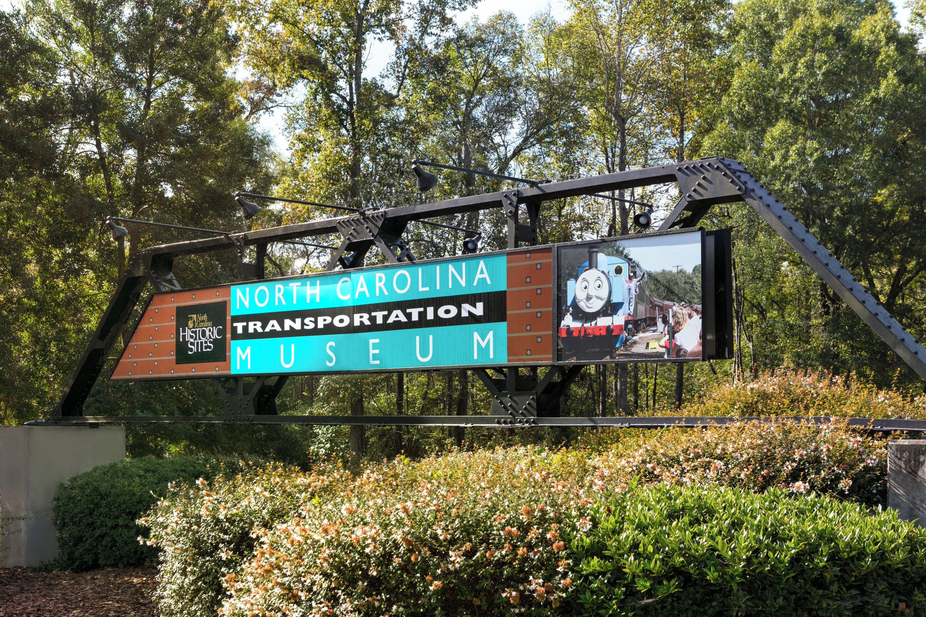 A signboard for the North Carolina Transportation Museum with a depiction of a train and Thomas the Tank Engine.