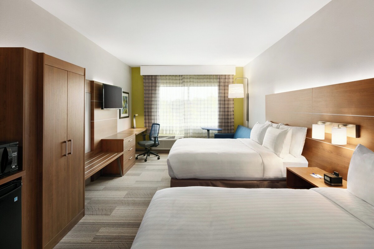 Een hotelkamer met twee bedden, een bureau, een stoel, een televisie en een raam met gordijnen.