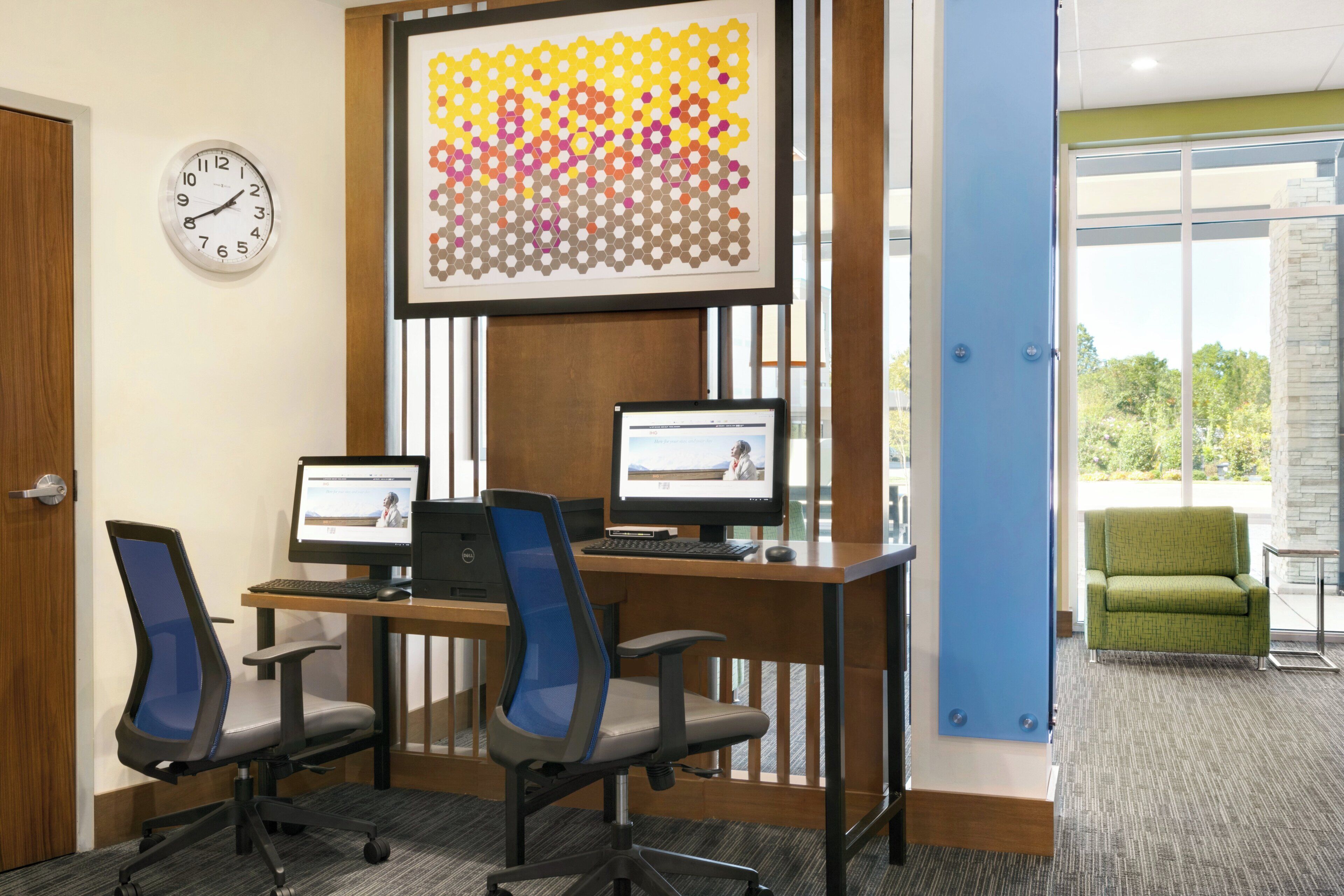 A conference room with two desks, two chairs, a clock, and a large abstract artwork on the wall.
