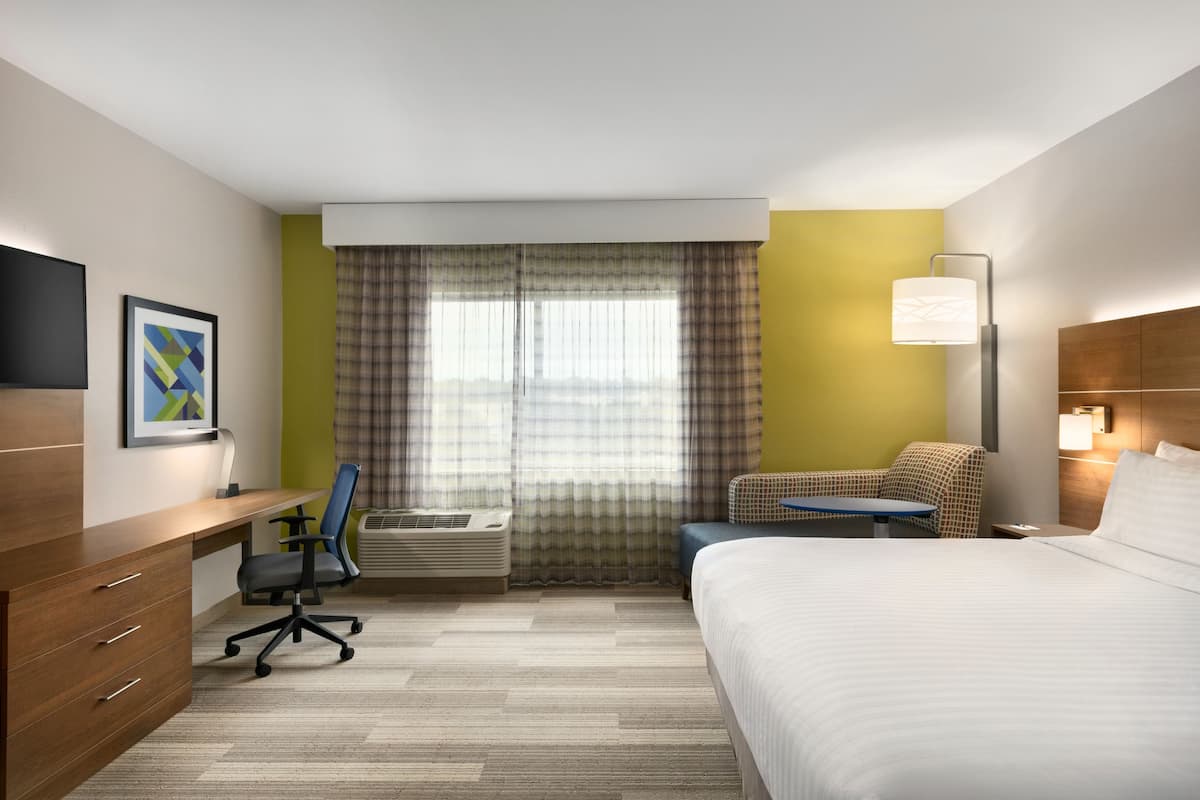 Habitación de hotel con cama, escritorio, silla, aire acondicionado y ventana con cortinas.