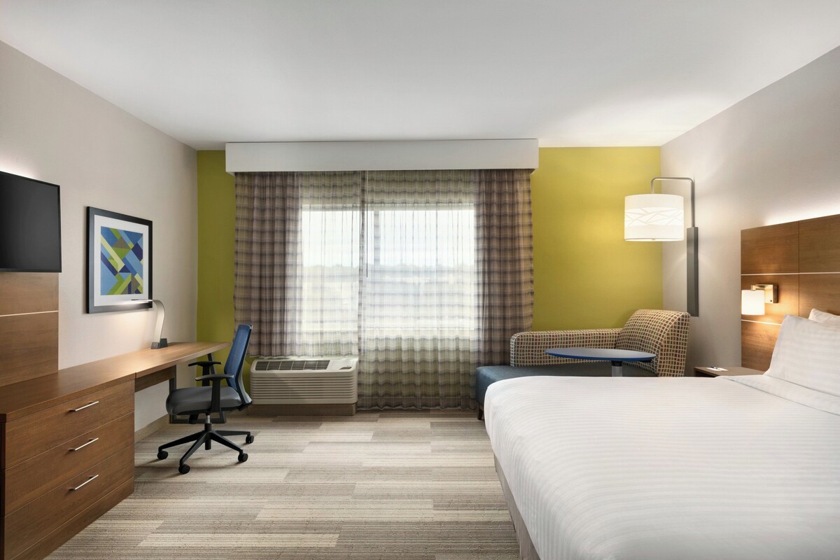 Hotelkamer met een bed, bureau, stoel, airconditioning en een raam met gordijnen.