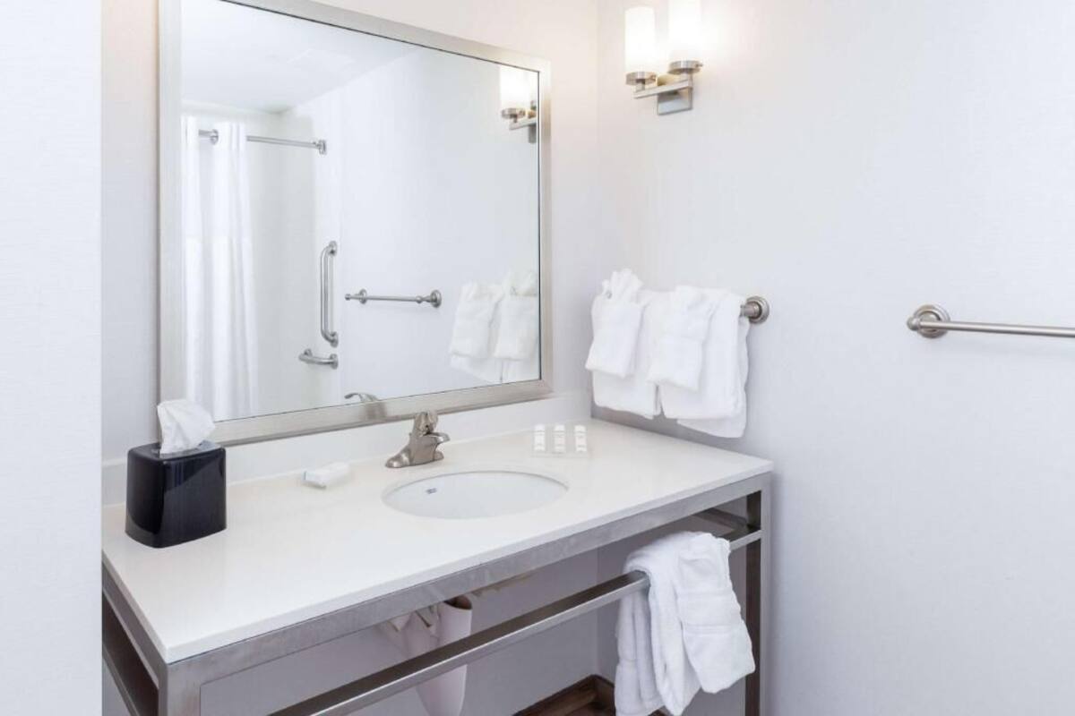 A bathroom with a large mirror, a sink, a towel rack, and a handrail.