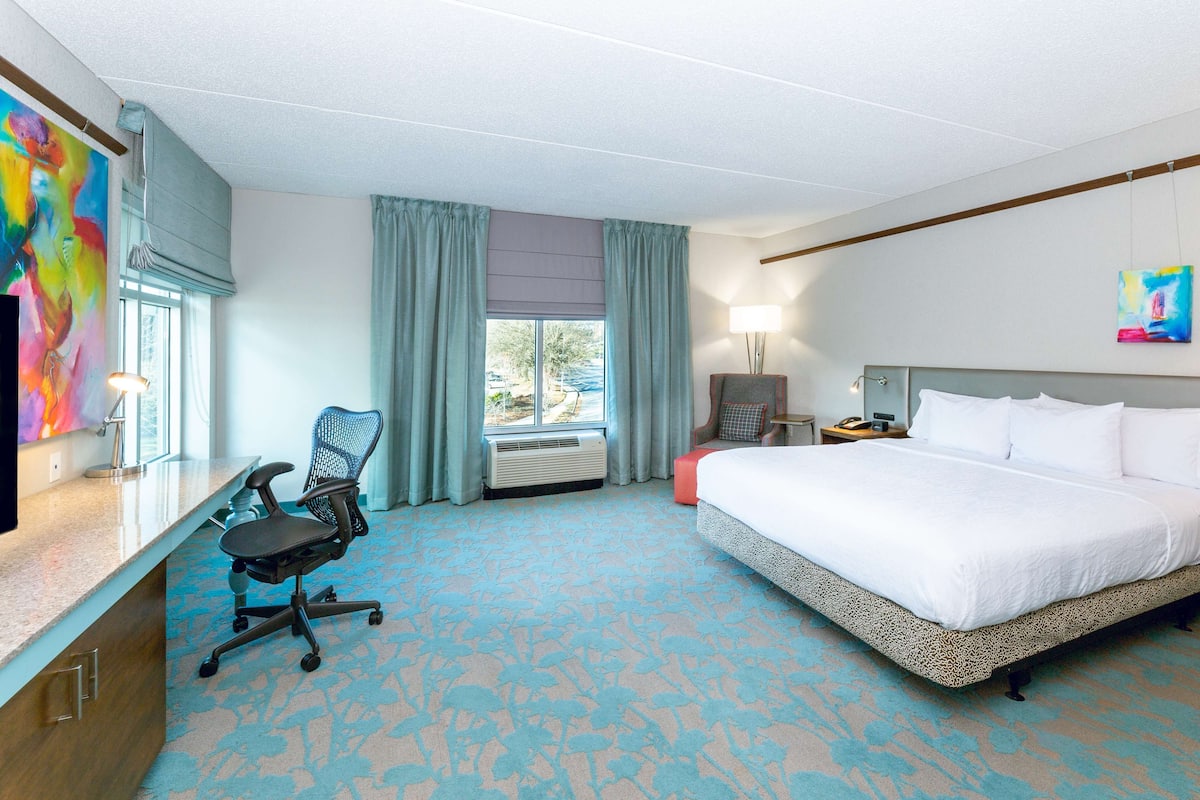 A hotel room with a bed, desk, chair, and a window with curtains.