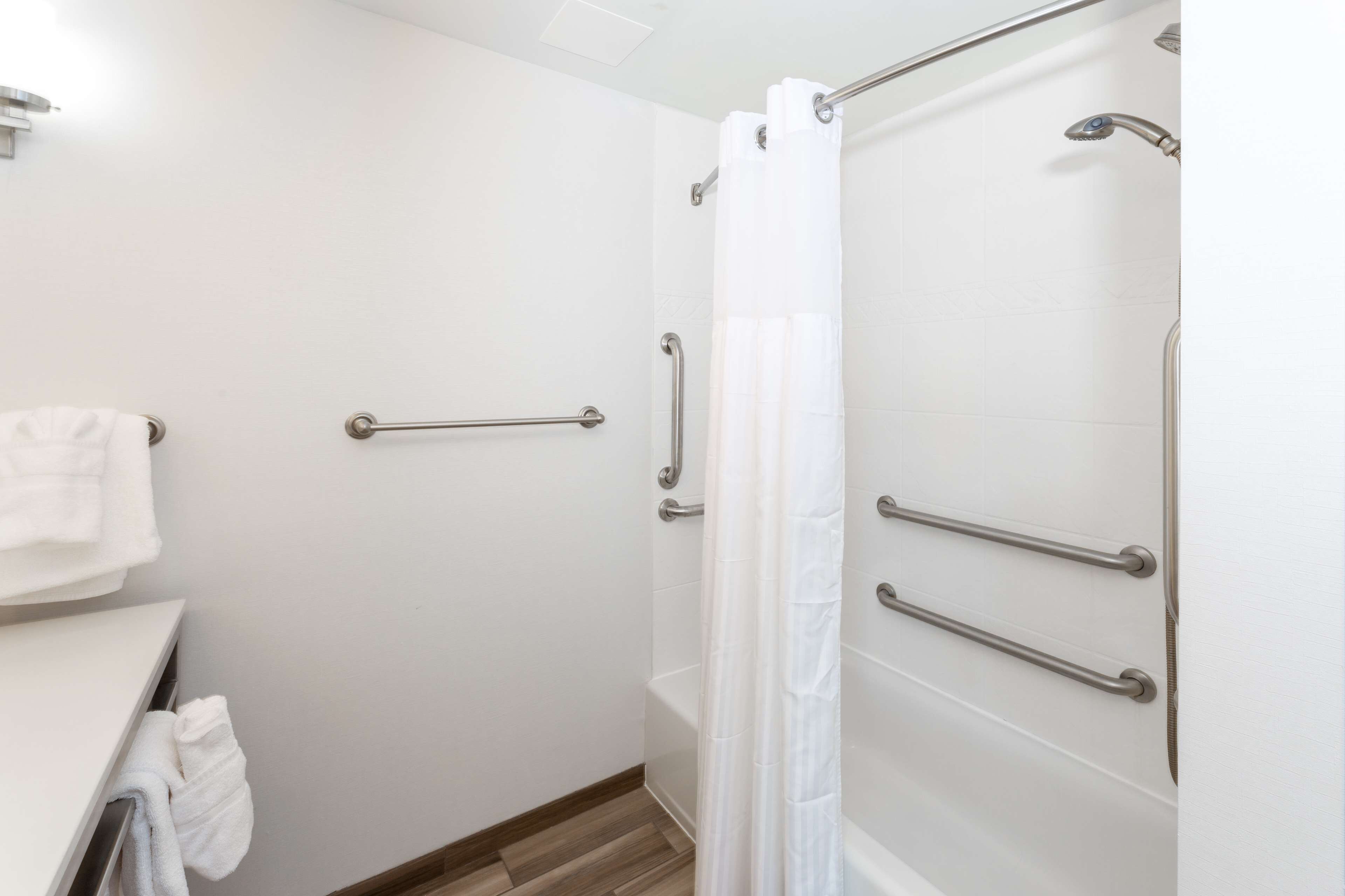 A bathroom with a shower, grab bars, and a towel rack.
