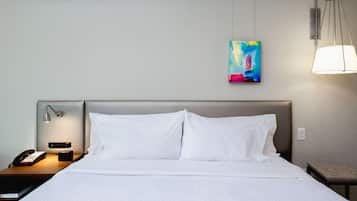 A hotel room with a large bed, a bedside table with a lamp, a phone, and a painting on the wall.