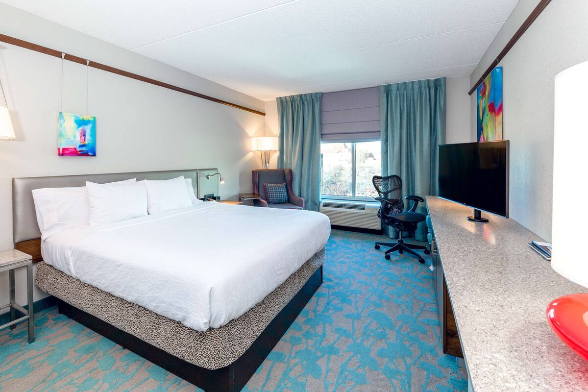 A hotel room with a large bed, a desk with a computer, a TV, and a chair.