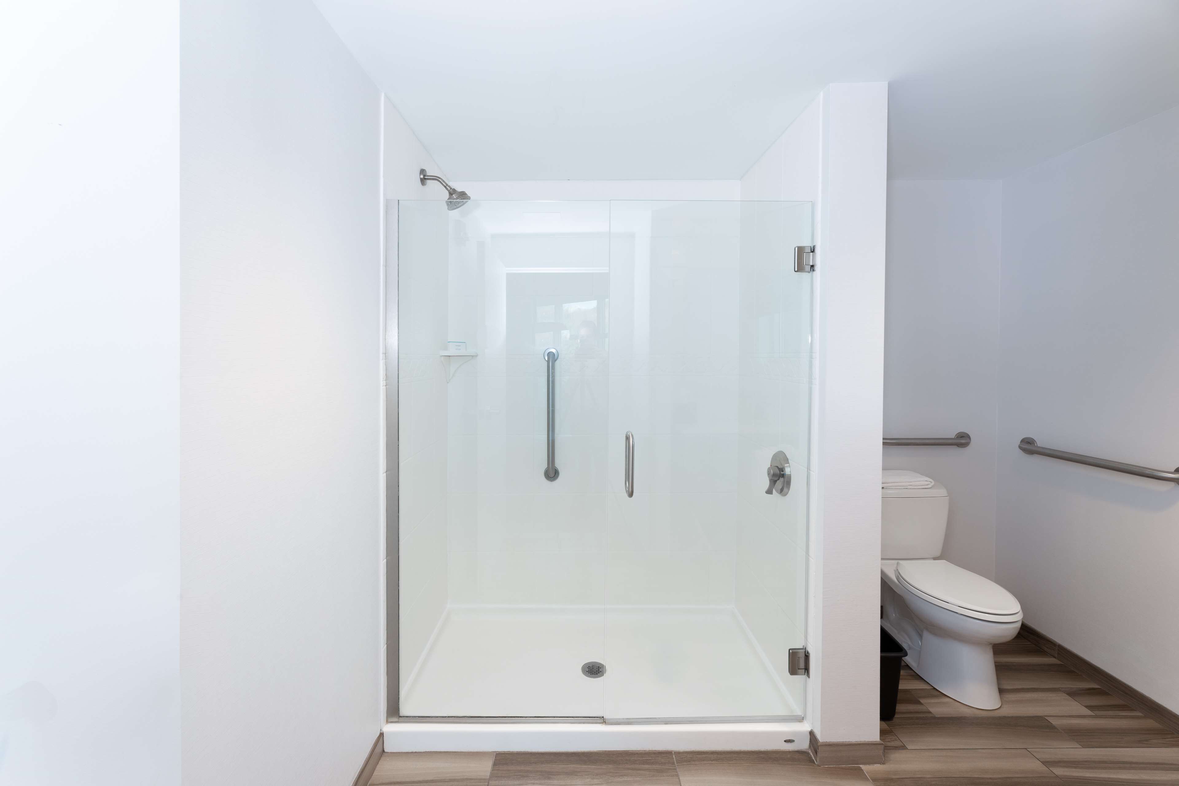 Une salle de bain moderne avec une douche à parois de verre, des toilettes blanches et un plancher en bois.