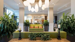 Un vestíbulo con un sofá verde, plantas en macetas y un candelabro.