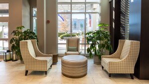 Un hall d’entrée avec deux fauteuils, un pouf rond et des plantes en pot.